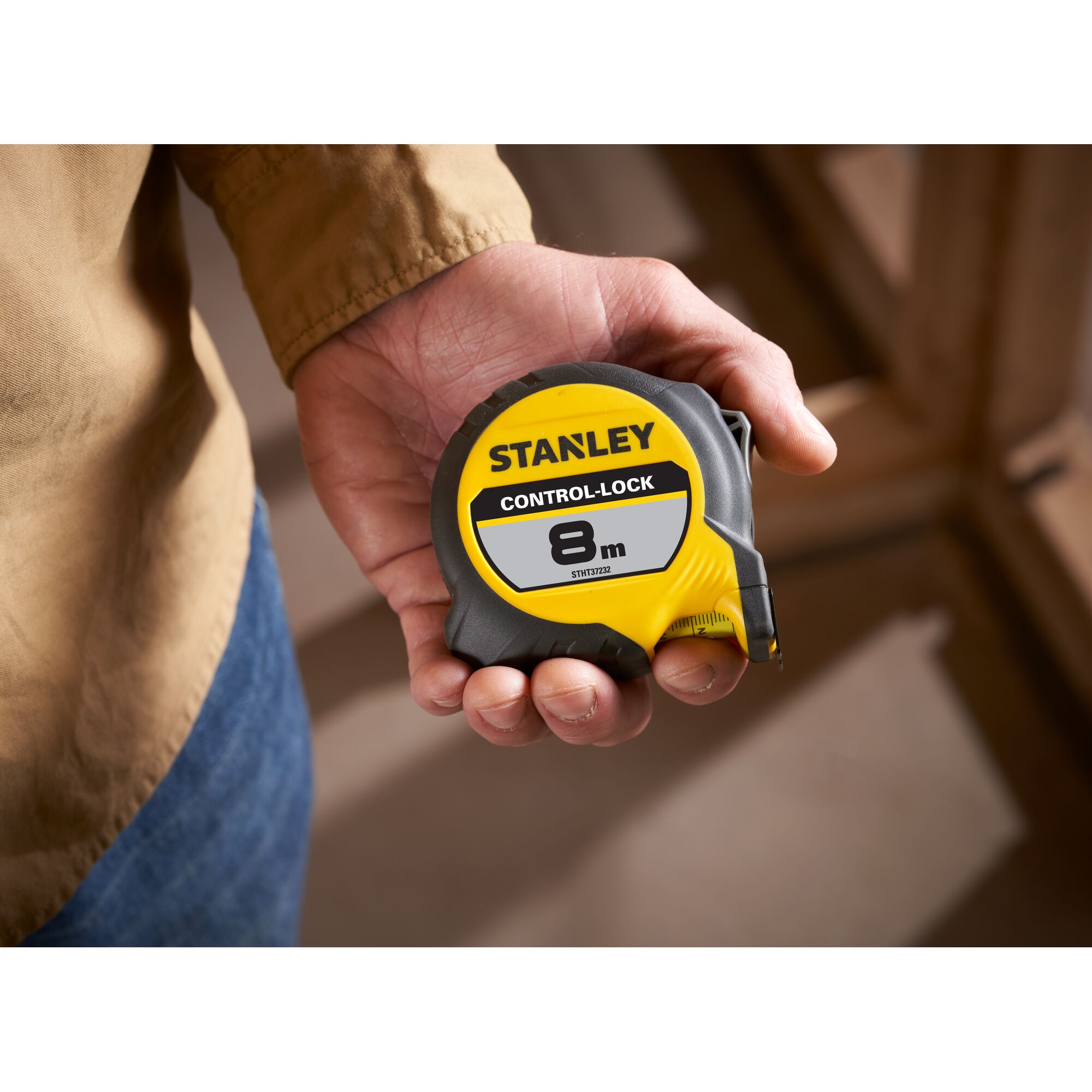STANLEY STHT37232 tape measure, yellow and black, 8m CONTROL-LOCK, held in hand, product photography.